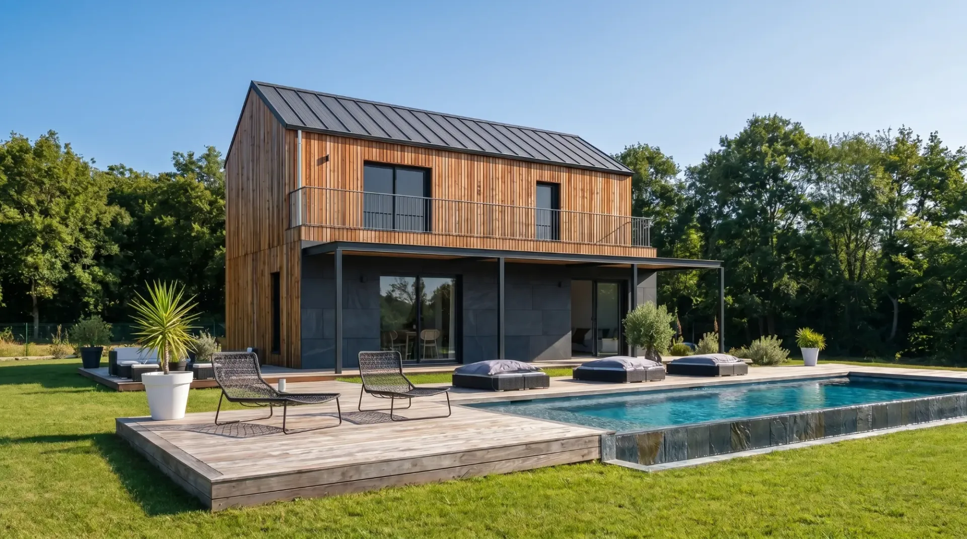 Maison Greenkub en ossature bois à étage, bardage bois et soubassement anthracite, terrasse en bois et piscine sous un ciel bleu