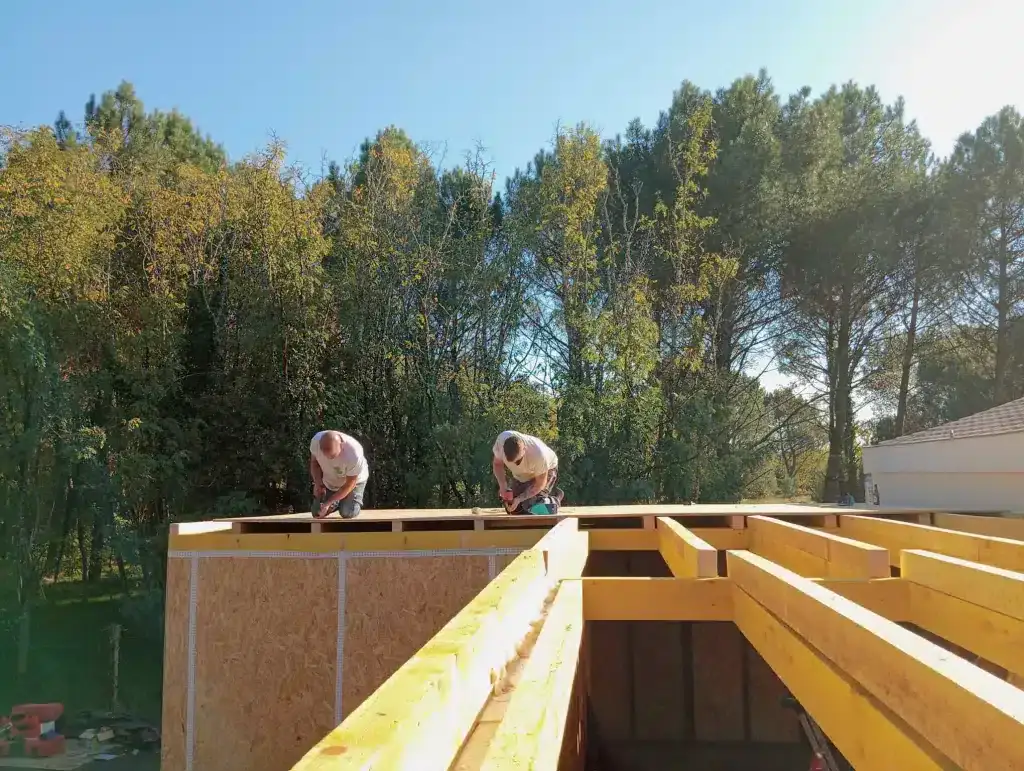 Deux charpentiers vissent les solives sur les murs à ossature bois d'une maison en cours de montage