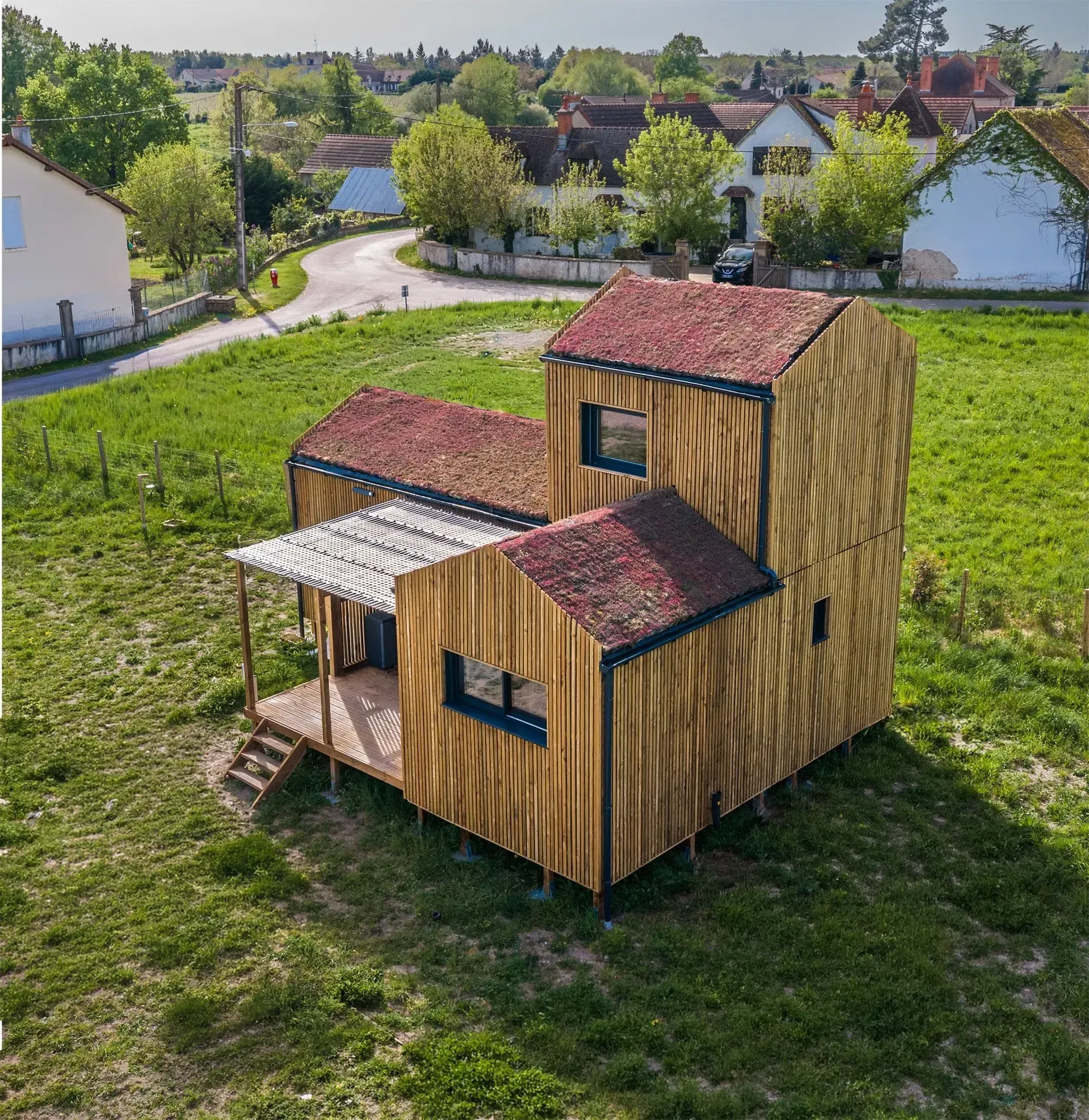 Vue aérienne d’une maison bois Greenkub GK50 en Allier · composition de trois volumes bardage bois vertical avec toitures végétalisées, terrasse centrale couverte, environnement rural