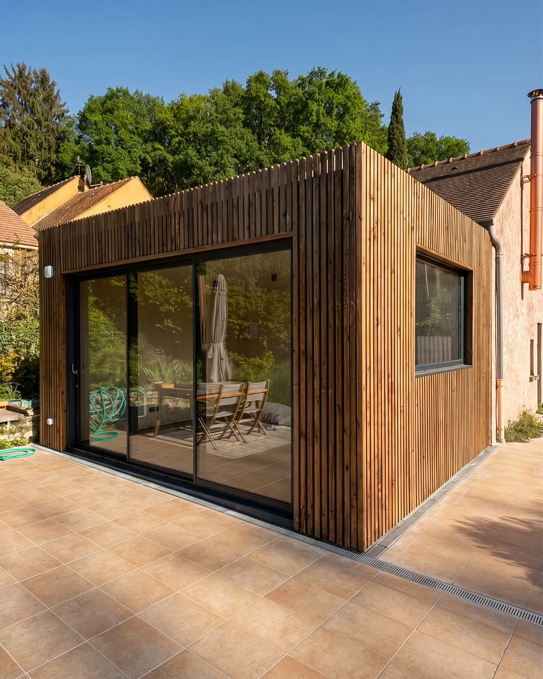 Extension de maison en ossature bois à toit plat accolée à une maison en pierre, grande baie coulissante ouverte sur la terrasse