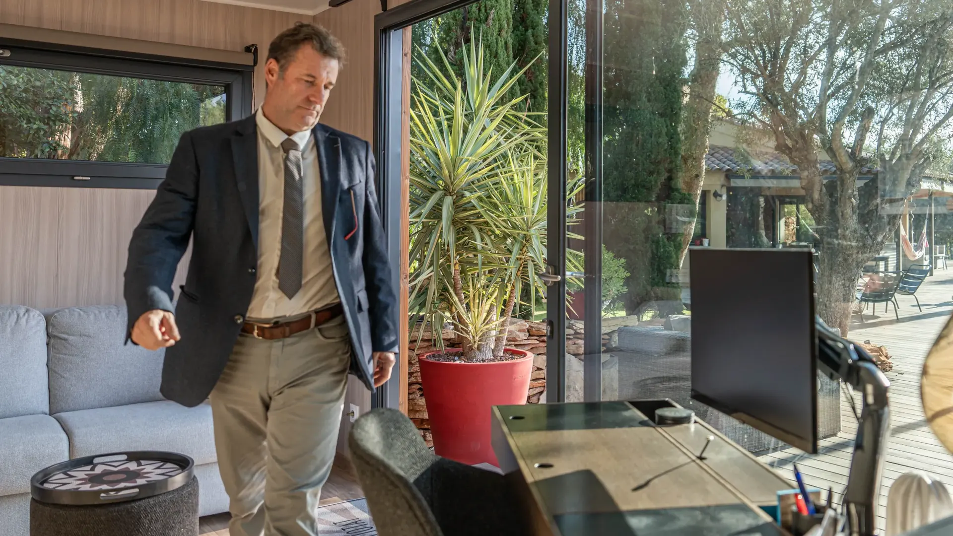 Studio de jardin Greenkub aménagé en bureau : poste de travail, écran et canapé devant les baies vitrées ouvertes sur le jardin
