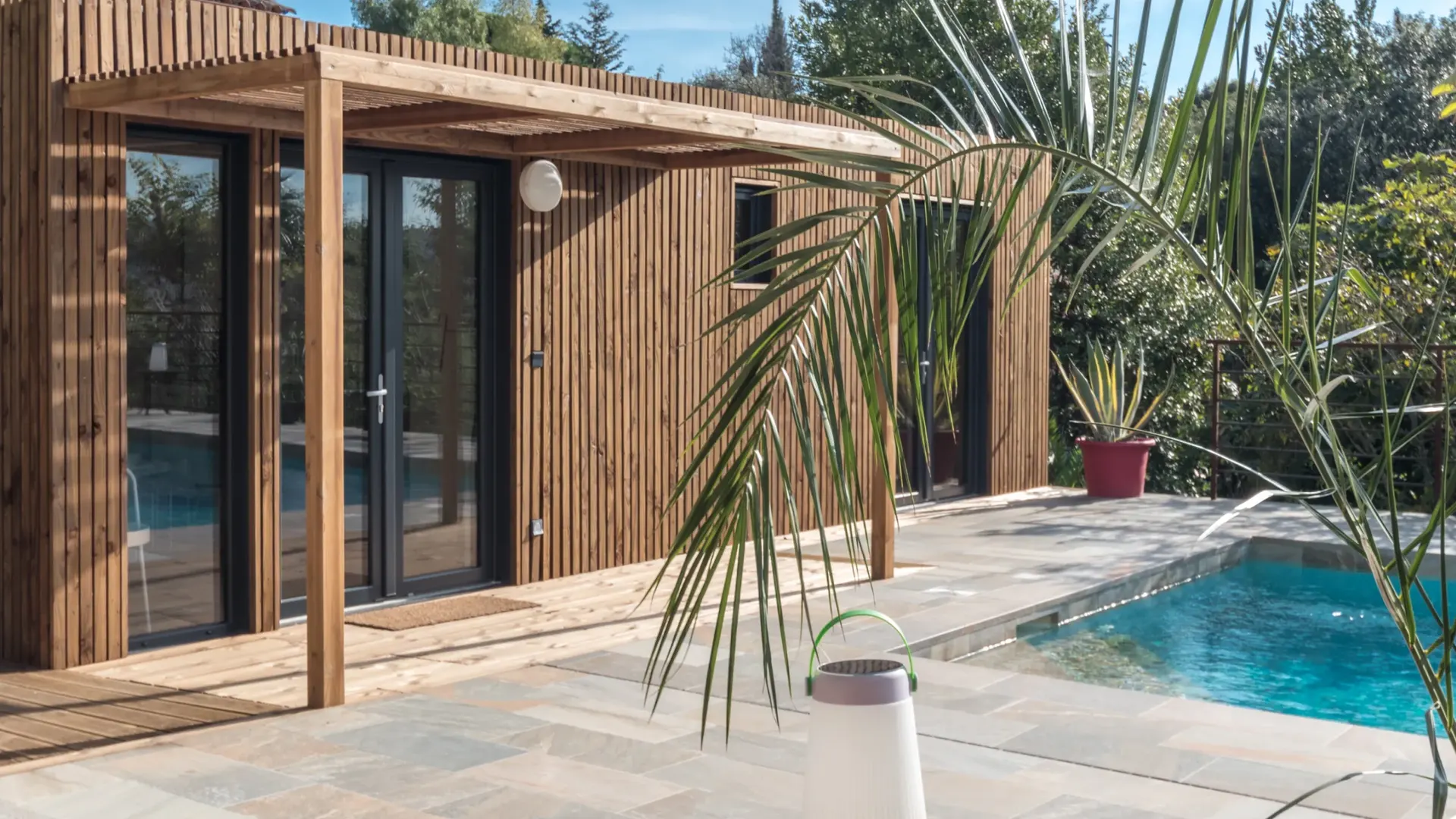 Pool house Greenkub GK30 en ossature bois, pergola et terrasse en pierre au bord de la piscine