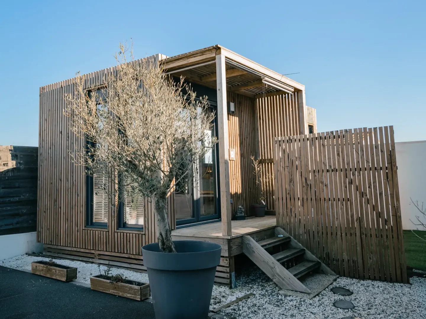 Pool house Greenkub GK20 de 20 m² : terrasse en bois, parasol et baie vitrée ouverte sur le jardin