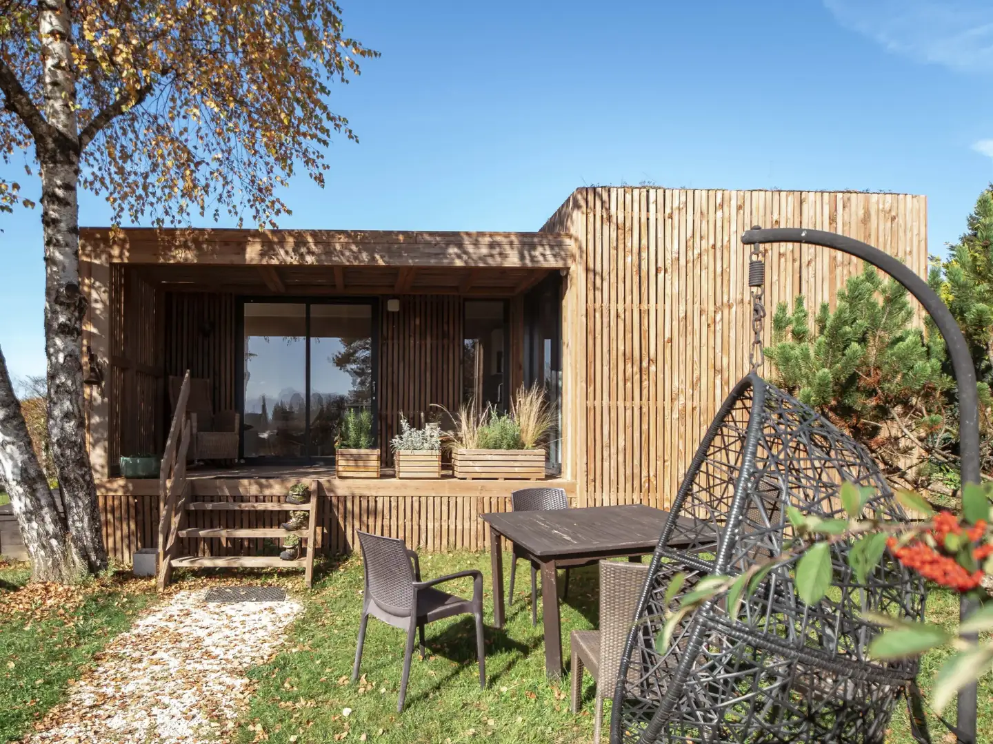 Studio de jardin Greenkub GK30 en ossature bois sous un ciel d'automne, auvent, terrasse et salon de jardin