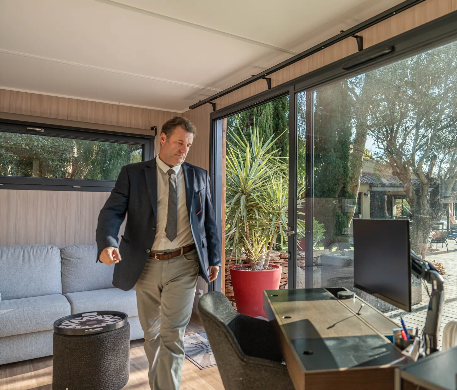 Studio de jardin aménagé en bureau : poste de travail, écran et fauteuil, grande baie vitrée coulissante ouverte sur le jardin