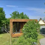 Studio de jardin en bois derrière un petit arbuste