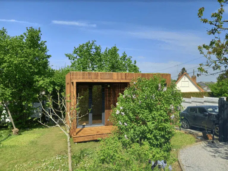 Studio de jardin en bois derrière un petit arbuste