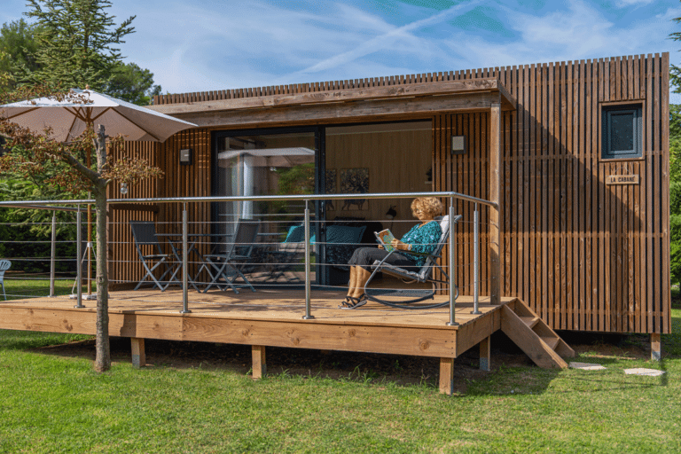Une maison en bois avec une femme lisant un livre sur sa terrasse