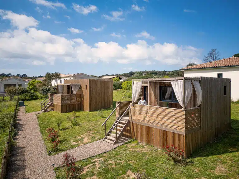 Deux studios modulaires Greenkub GK20 installés sur un terrain en pente végétalisé, bardage bois et rideaux blancs