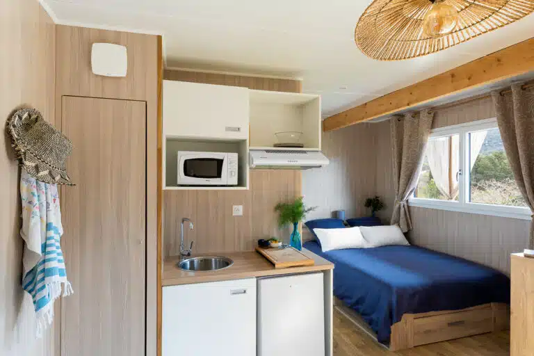 Lumineux intérieur d'un Greenkub GK20 en location : fenêtre double vantail, rideaux lin et literie bleue