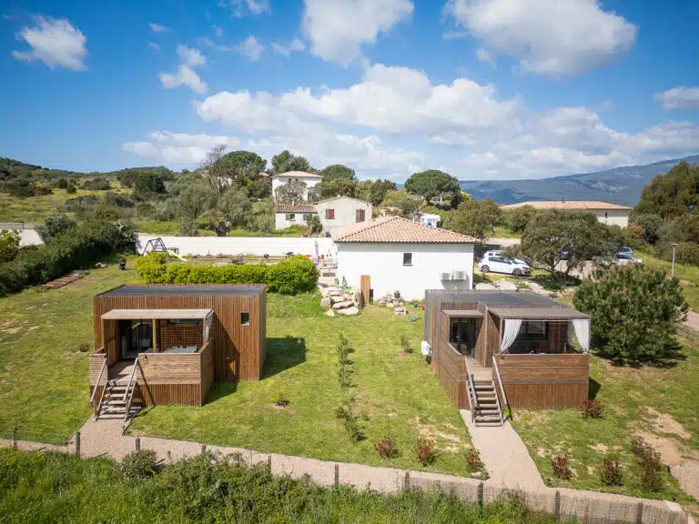 Vue d'ensemble d'un village de studios Greenkub GK20 avec allée gravillonnée et clôture bois traditionnelle