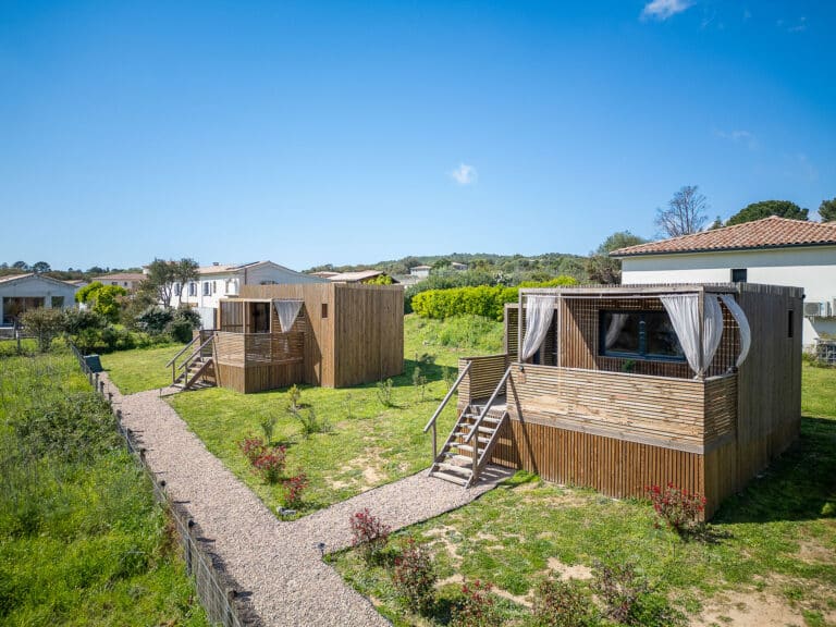 Studio modulaire Greenkub GK20 posé sur pilotis bois, terrasse avec rideaux blancs flottants au vent