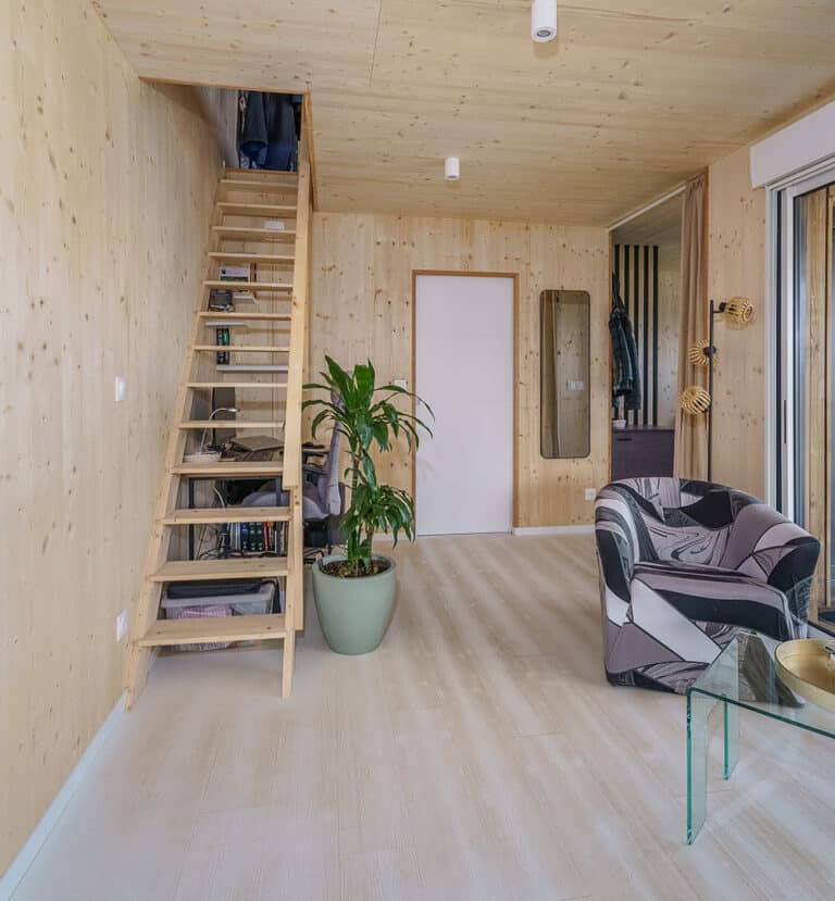 Intérieur maison modulaire 50m² avec mezzanine – murs bois massif, escalier en bois clair, lumière naturelle