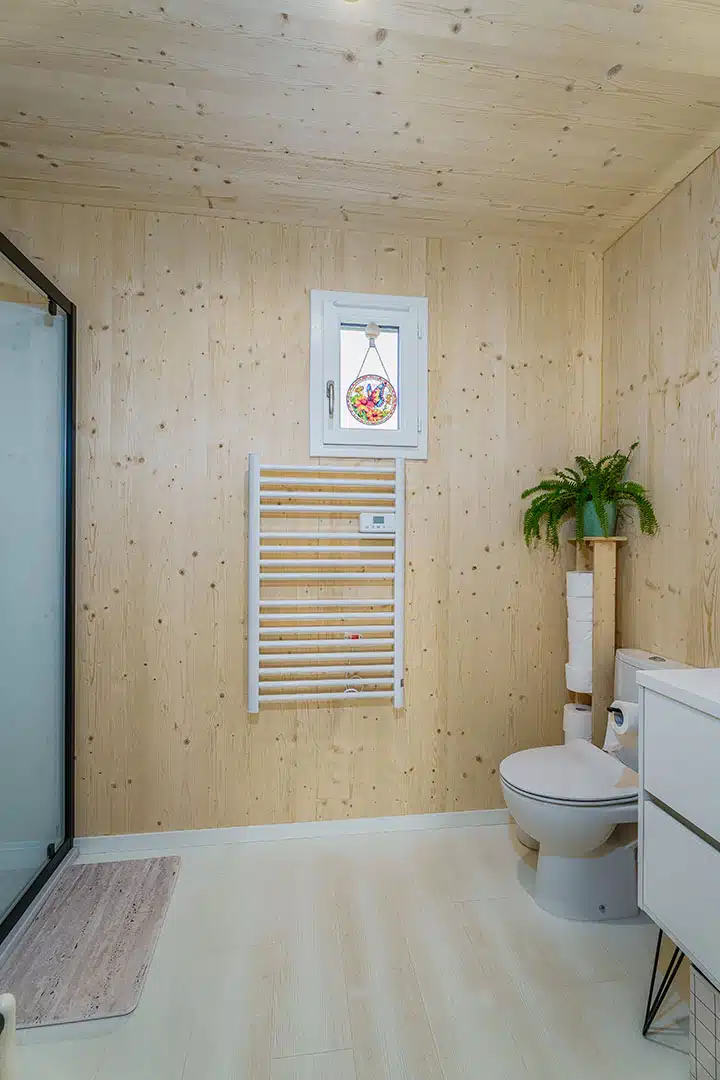 Salle d'eau compacte d'une maison modulaire bois Greenkub GK50 – parois en CLT épicéa naturel, vasque à poser blanche, miroir rétroéclairé, WC suspendu