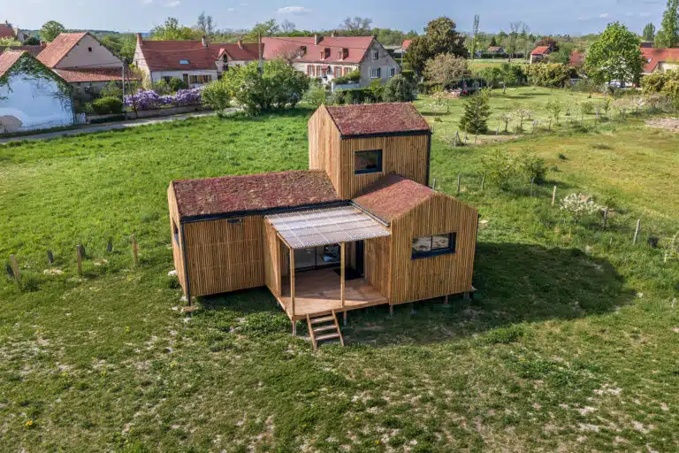 Vue aérienne d'une maison modulaire bois Greenkub GK50 en Allier – composition de trois volumes bardage bois vertical avec toitures végétalisées, terrasse centrale couverte, environnement rural